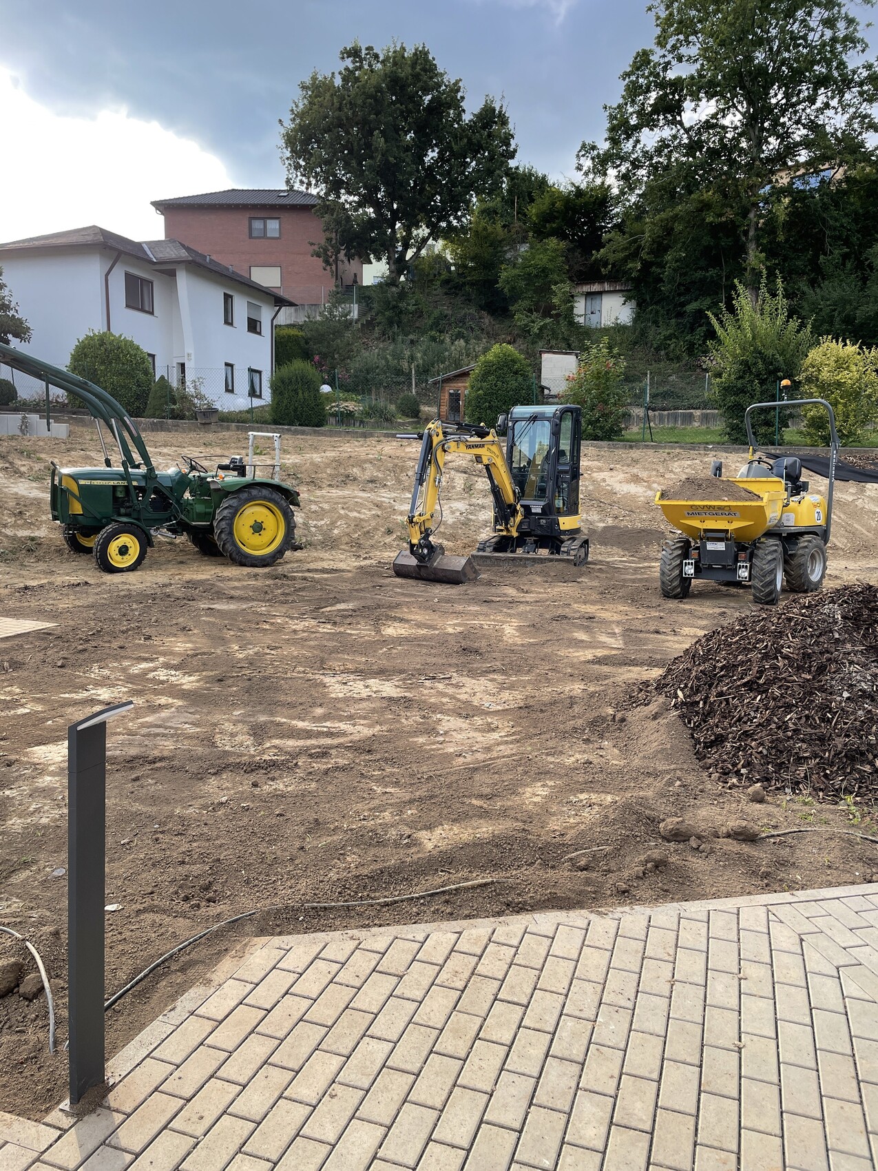 Baustelle mit gelbem Bagger in der Mitte, grünem Traktor links und gelbem Muldenkipper rechts.