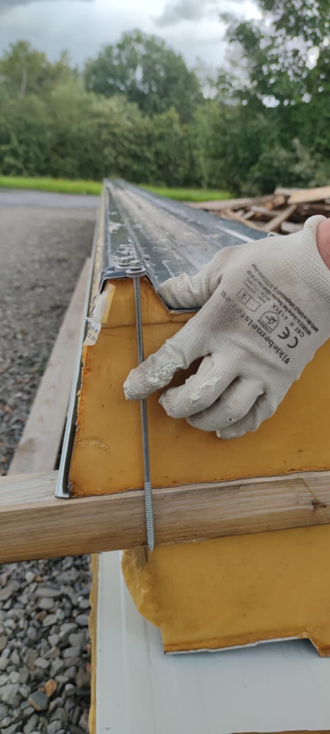 Hand mit Arbeitshandschuhen montiert Metallwinkel an gelbem Bauelement, Baugelände im Hintergrund