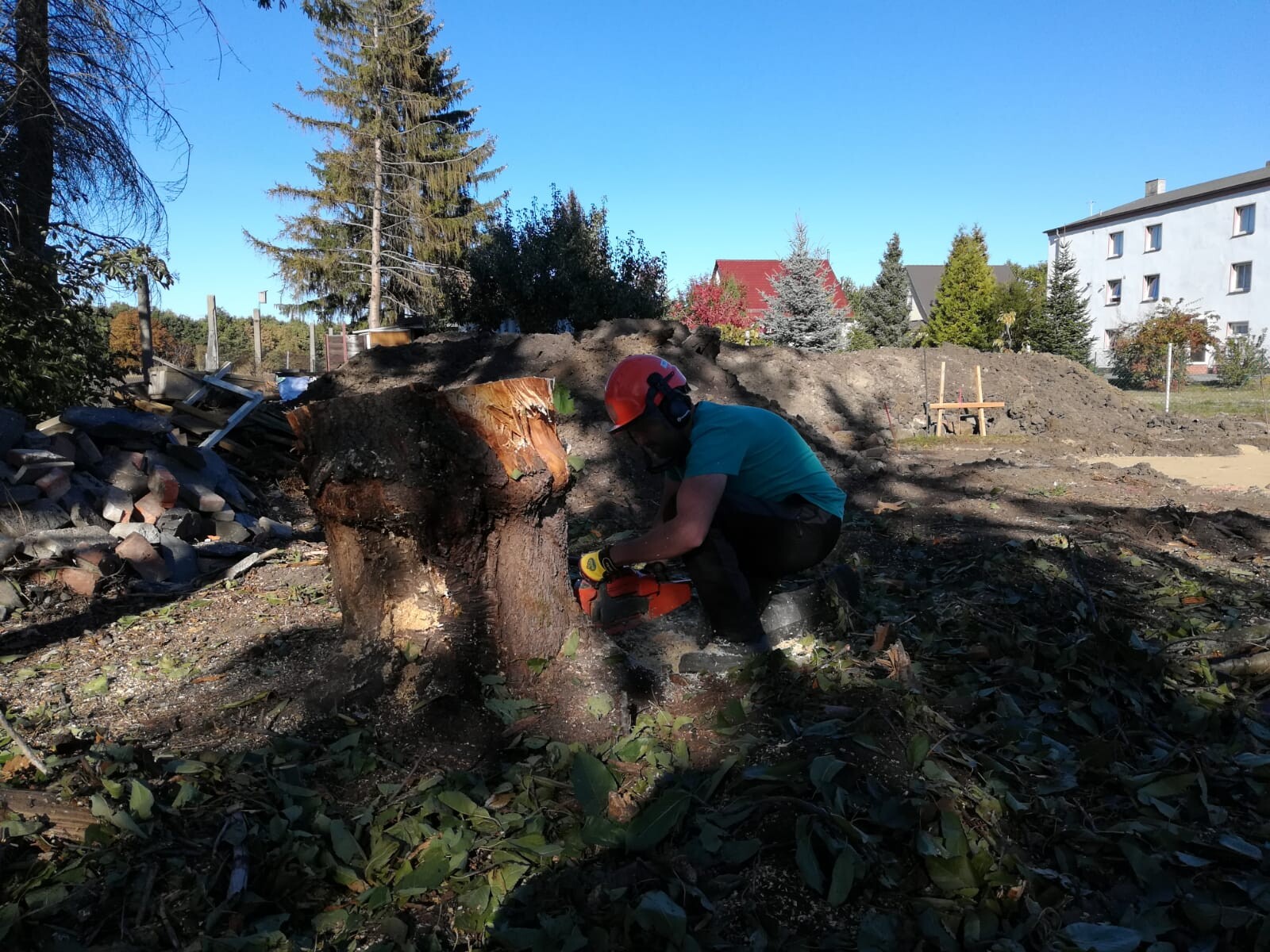 Bauarbeiter mit Helm entfernt Baumstumpf auf einer Baustelle im Freien