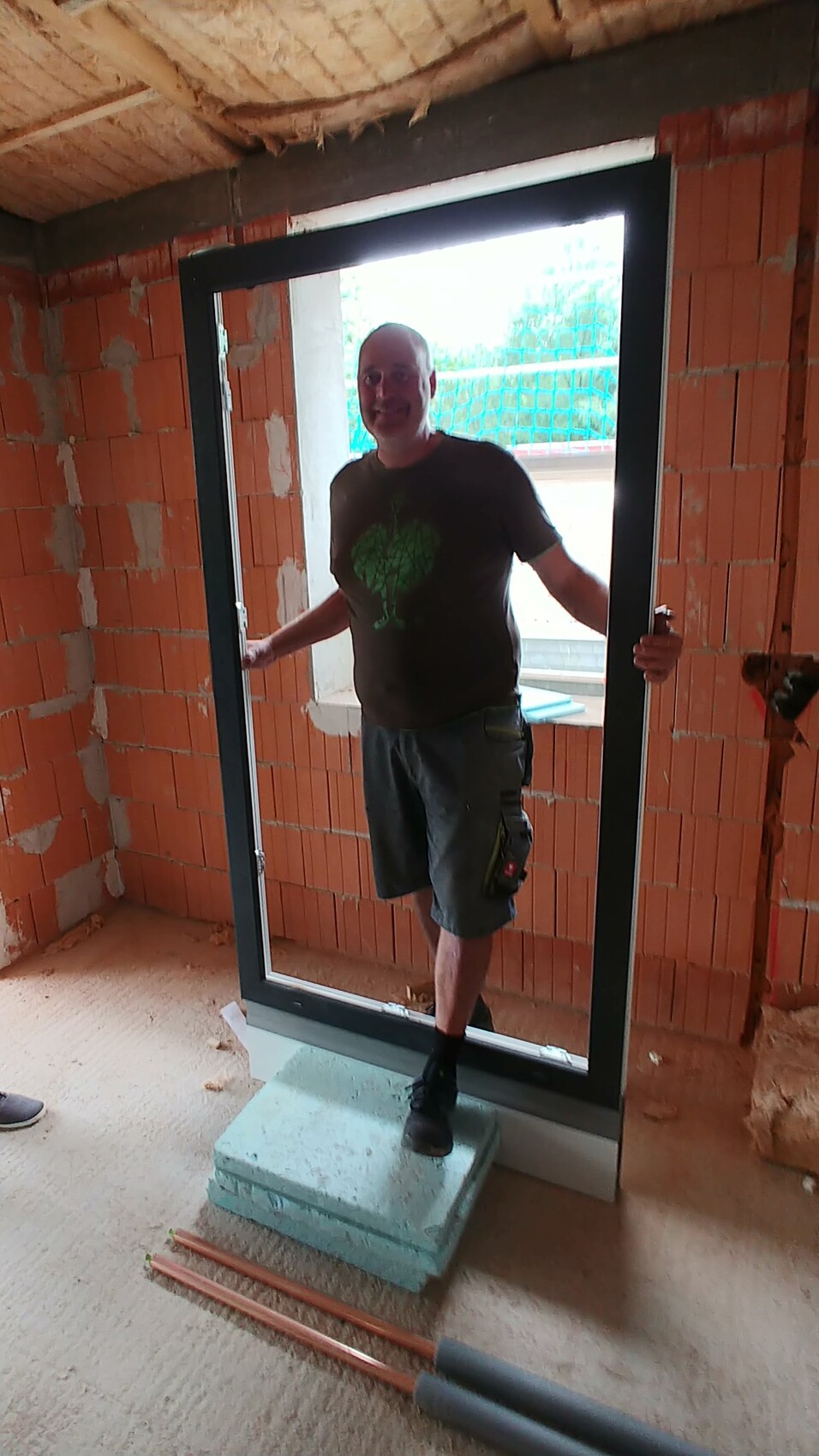 Mann steht in einem neu installierten Türrahmen eines Rohbaus, Baustelle sichtbar.
