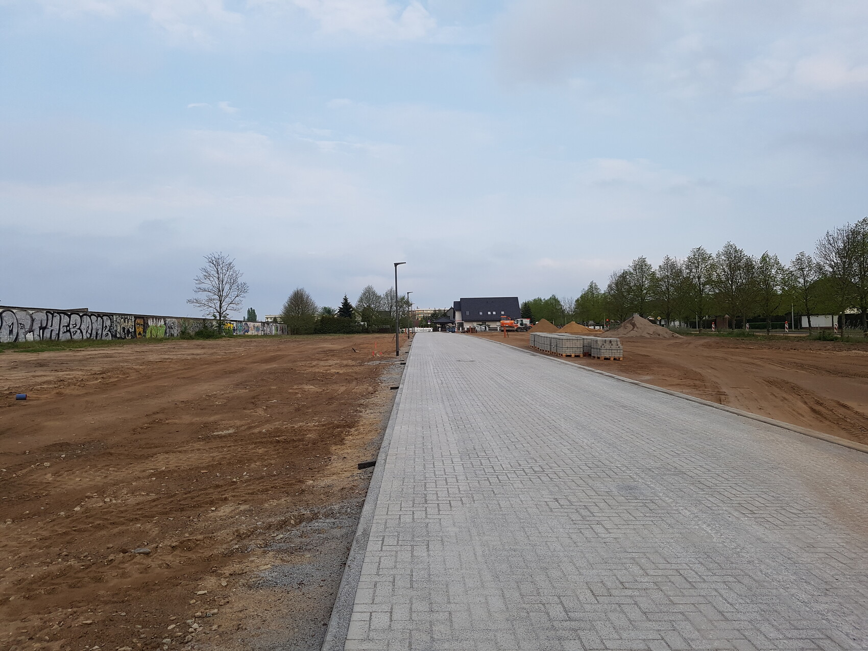 Pflasterweg auf einer Baustelle führt ins Baugelände mit Erdarbeiten und Baufahrzeugen im Hintergrund