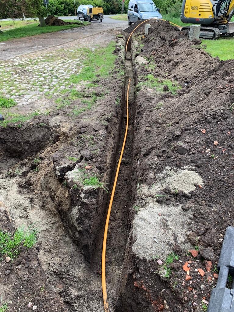 Tiefer Graben mit orangefarbenem Kabel, Baustelle an Straßenrand, Erdreich umgraben.