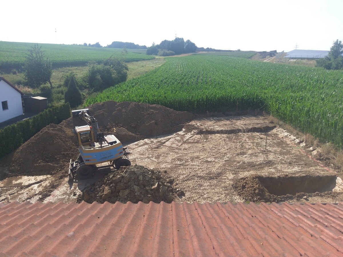 Bagger auf Baugrube auf offener Baufläche neben Feldern