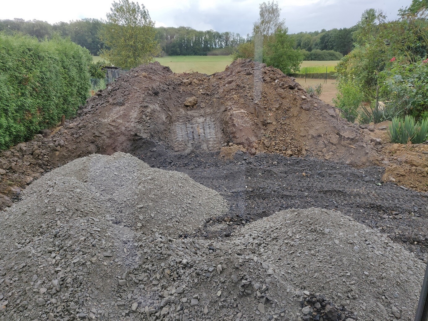 Große Erdmassen und Kieshaufen auf einer Baufläche mit Bäumen im Hintergrund