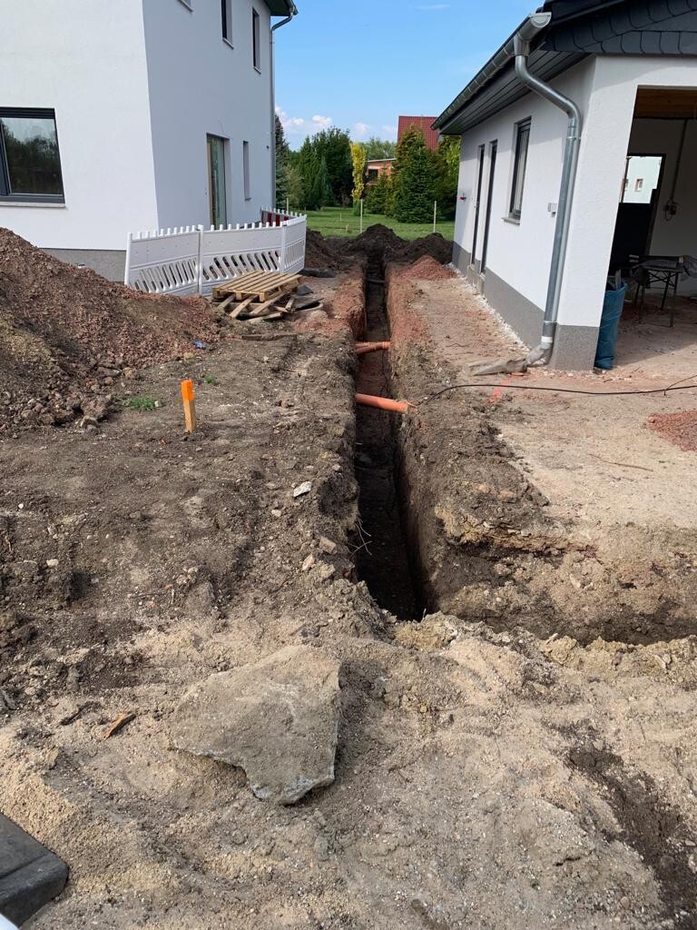 Graben zwischen zwei Häusern bei Bauarbeiten, sichtbare orangefarbene Rohre.
