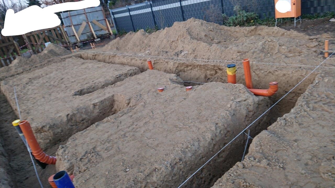Aushub im Garten: Baugrube mit orangefarbenen Abwasser-/Entwässerungsrohren, Vermessungsschnüre.