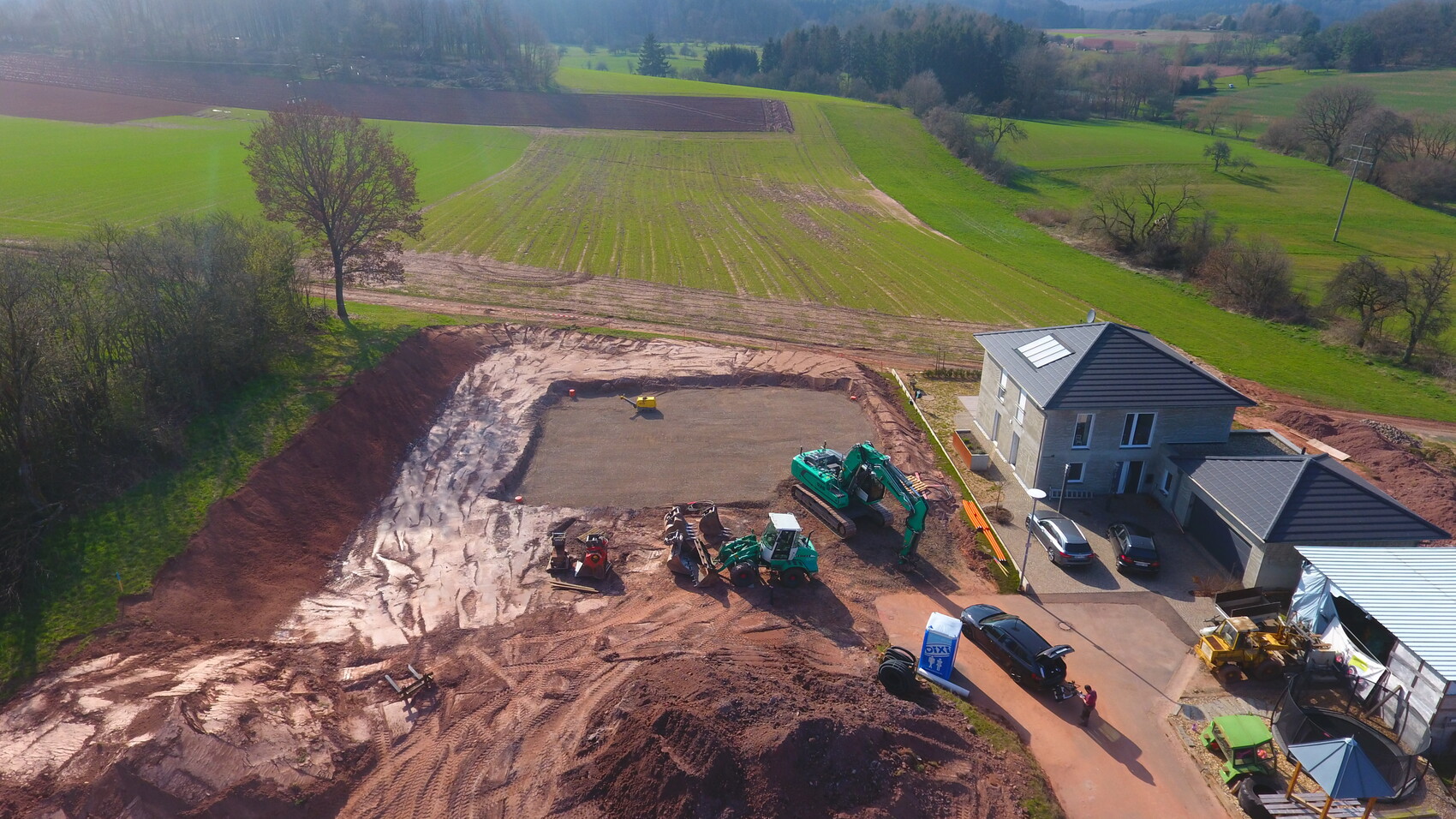 Luftaufnahme einer Baustelle neben einem Wohnhaus; Bagger, Erdaushub, Fahrzeuge