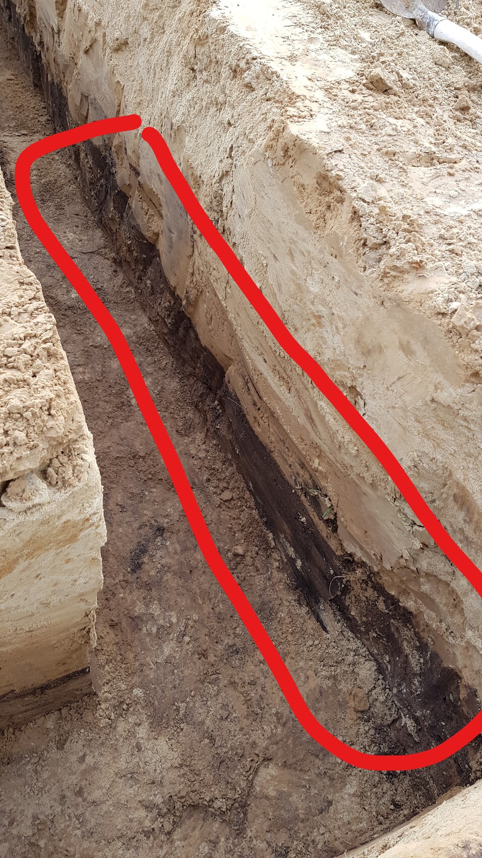 Ausgehobener Graben neben einer Fundamentwand mit loser Erde und dunklem Boden.