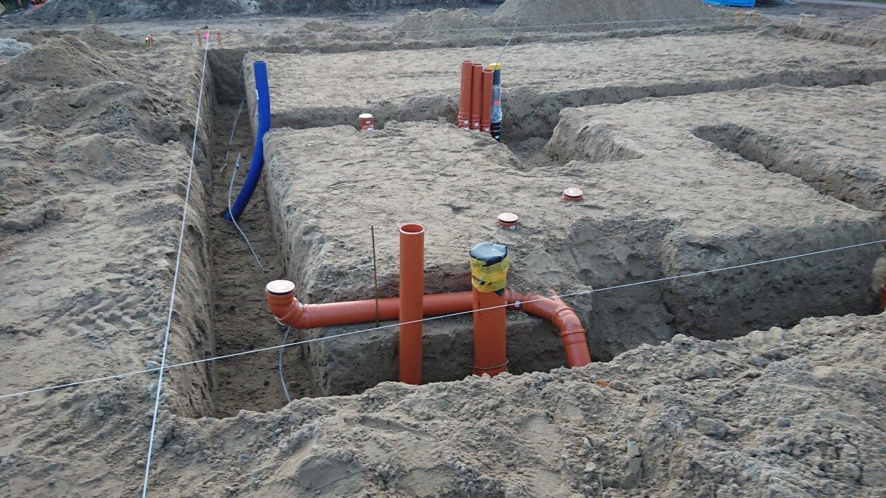 Baugrube mit orangefarbenen PVC-Rohren, blauem Flexschlauch, Erdarbeiten.