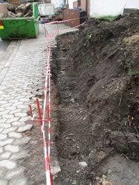 Baugrube neben gepflasterter Einfahrt mit Absperrband und Erdarbeiten