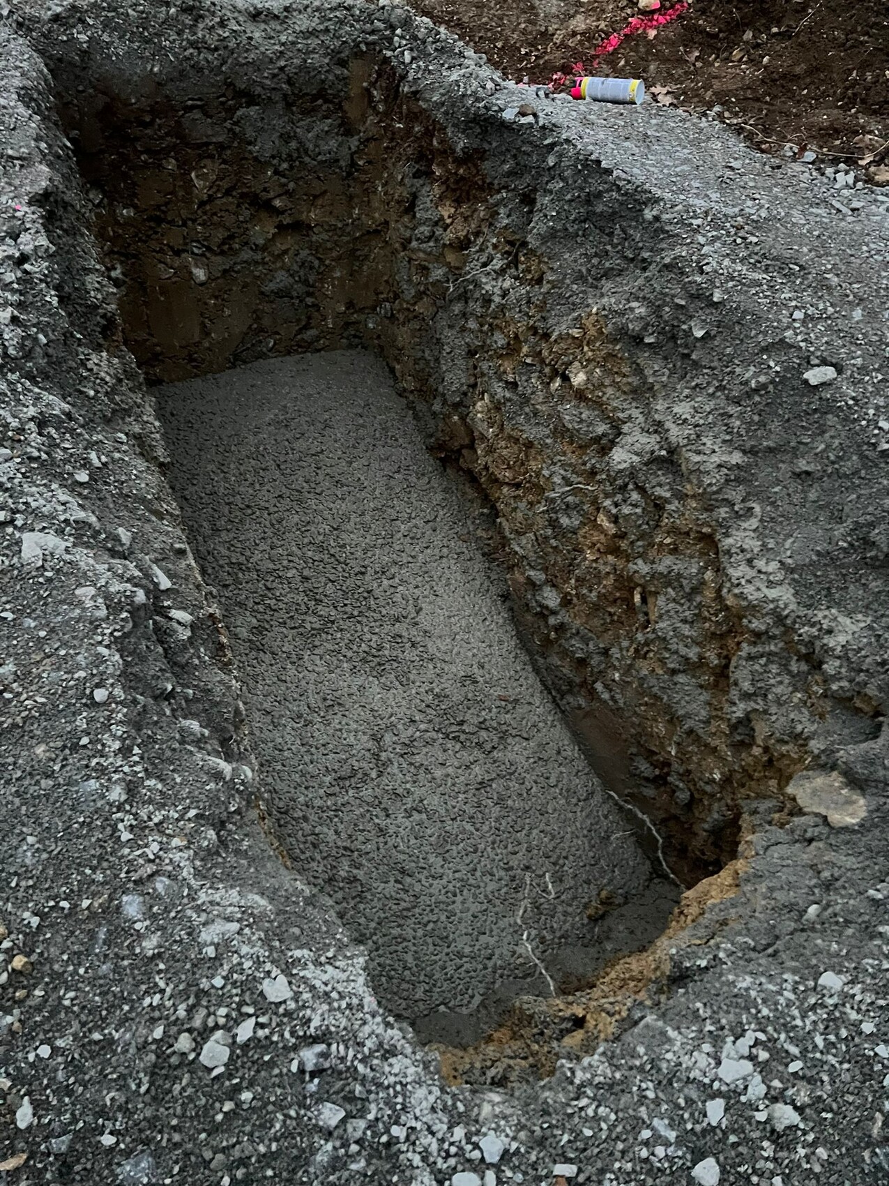 Tiefer Graben mit festem Kiesbetonboden, rundherum raues Erdreich auf einer Baustelle.