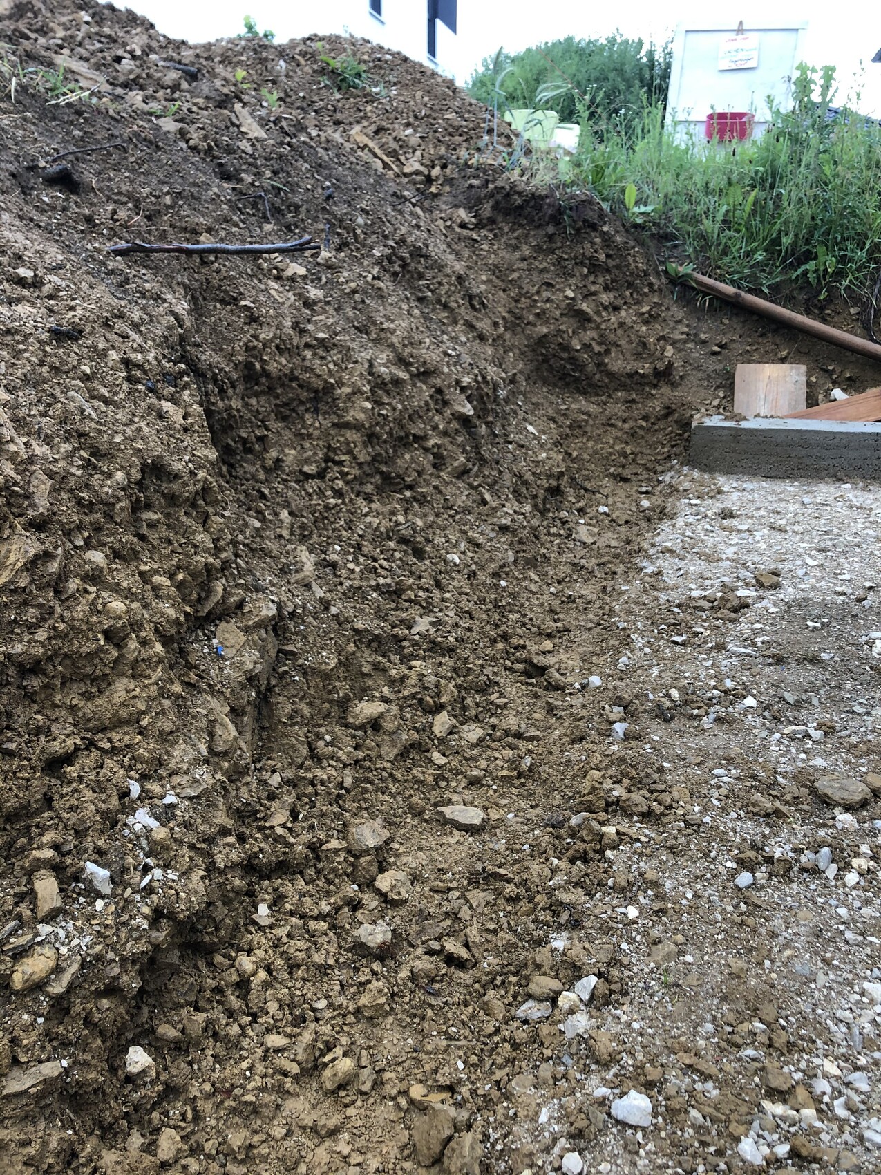 Großer Erdwall und Baugrube mit losem Boden, Schutt und Rohrleitungen auf Baustelle