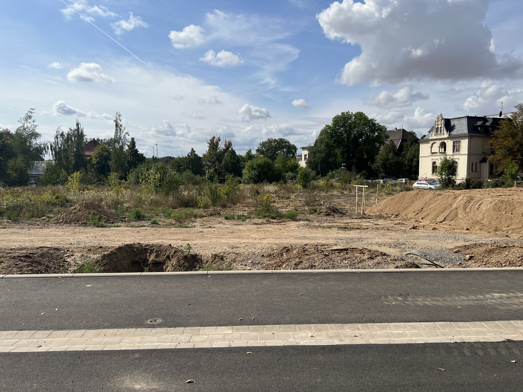 Rohbaustelle mit Erdarbeiten, Straßennähe im Vordergrund und Häuser im Hintergrund
