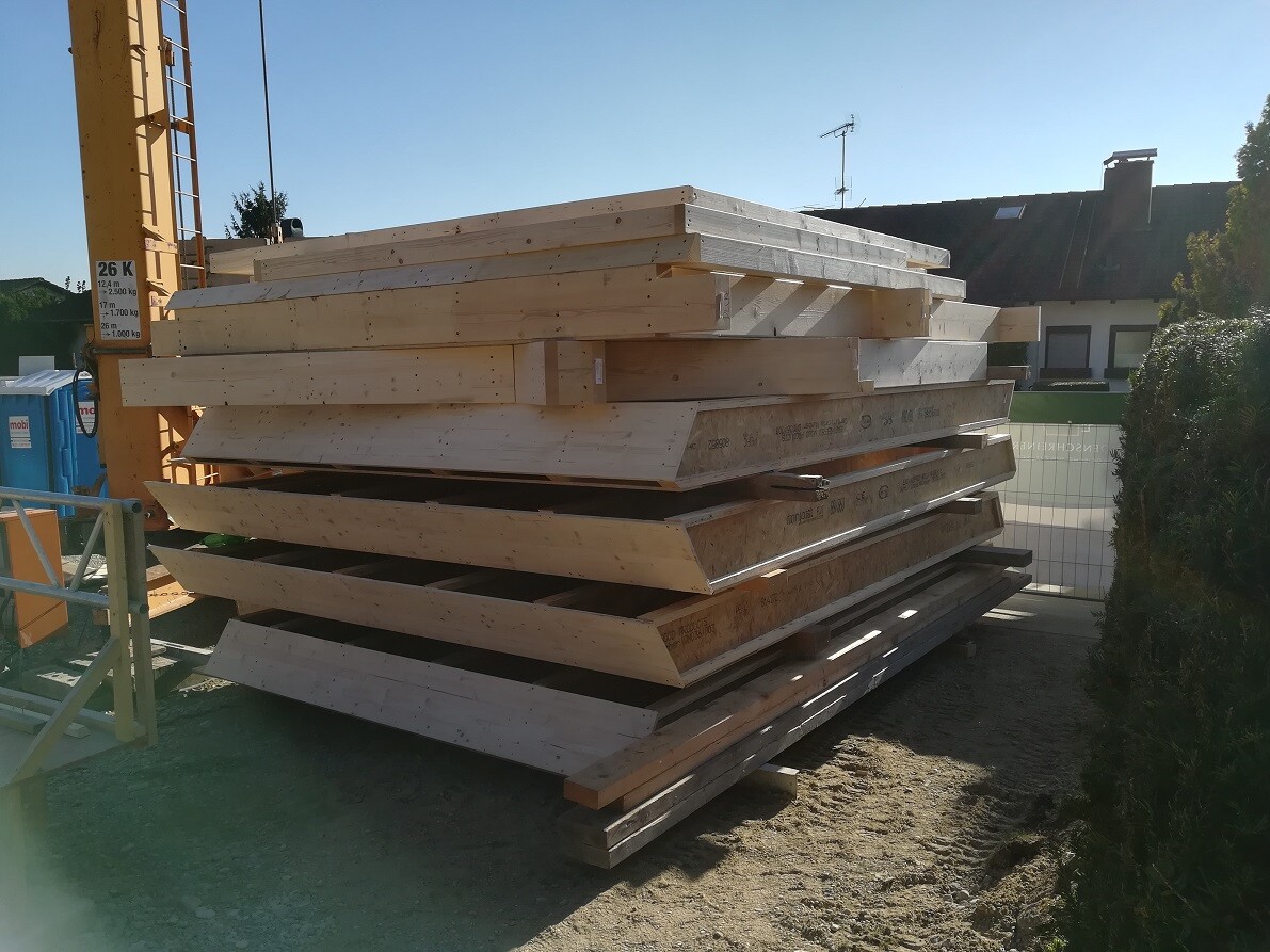Stapel roher Holzbalken und Bauholz auf Baustelle neben Haus