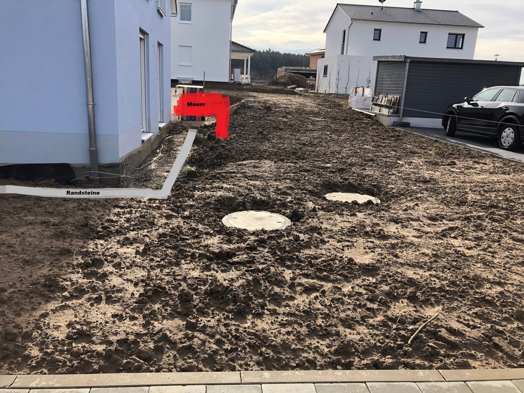 Baustelle vor Wohnhäusern: unbefestigte Erde, Randsteine, runde Deckel, rote Markierung 'Mauer'