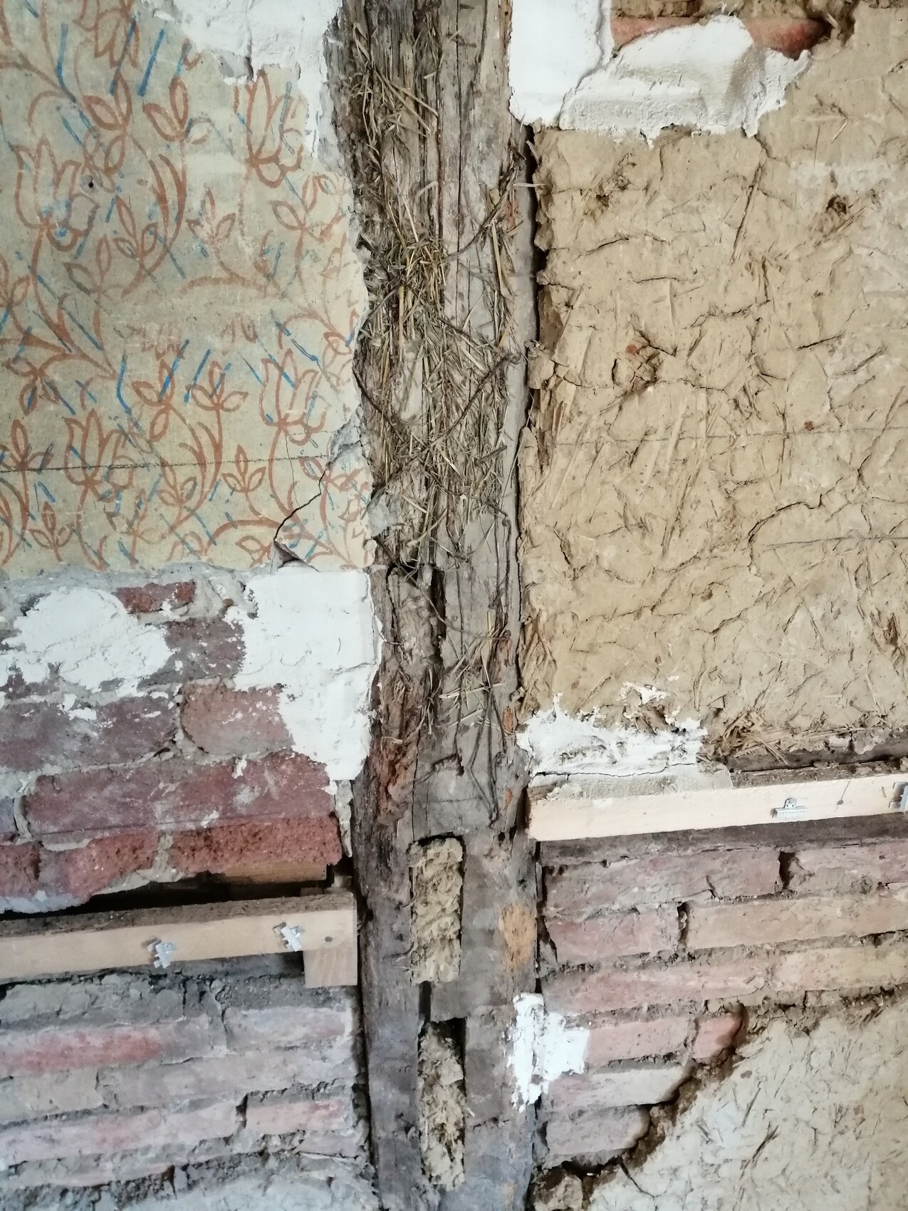 Alte, beschädigte Wand mit freiliegendem Strohgewerk und Putzresten.