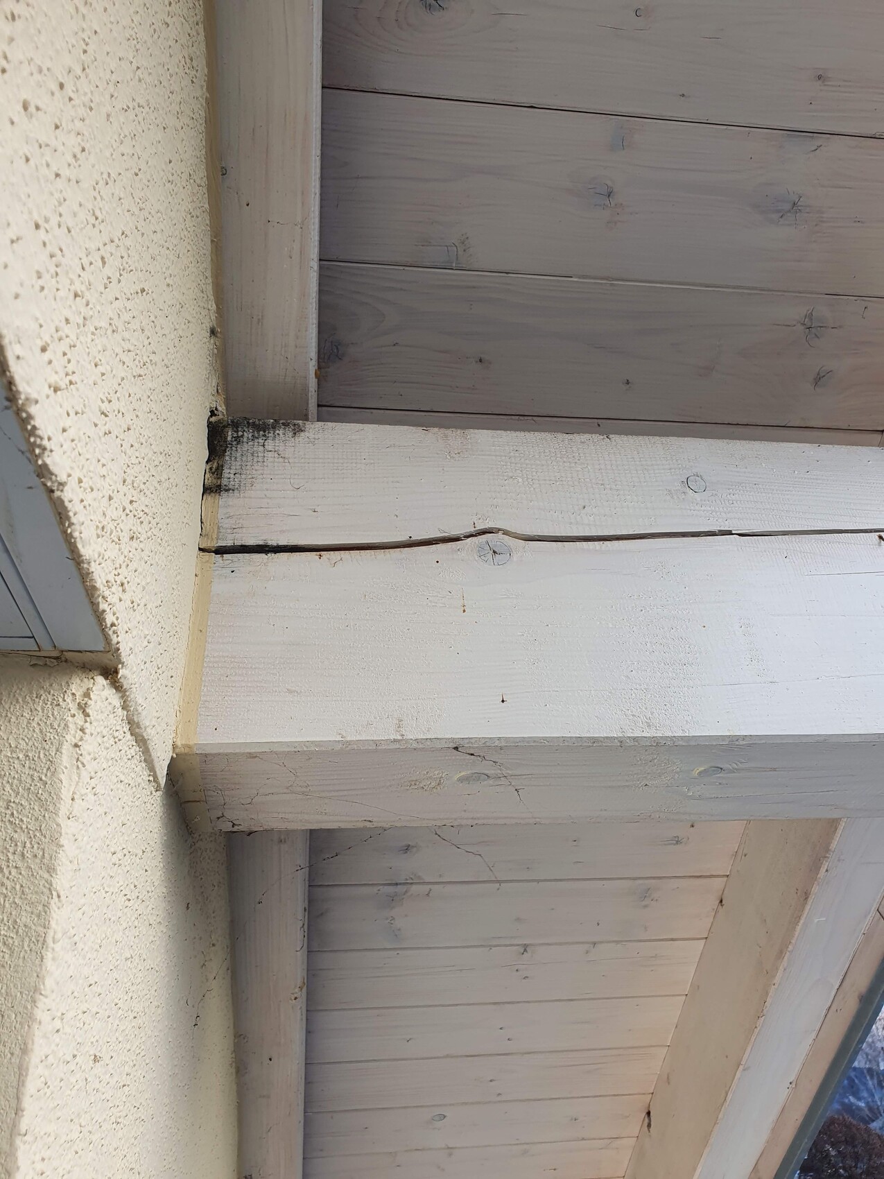 Außenansicht: Weiß gestrichener Holzbalken über verputzter Wand, Schrauben sichtbar.