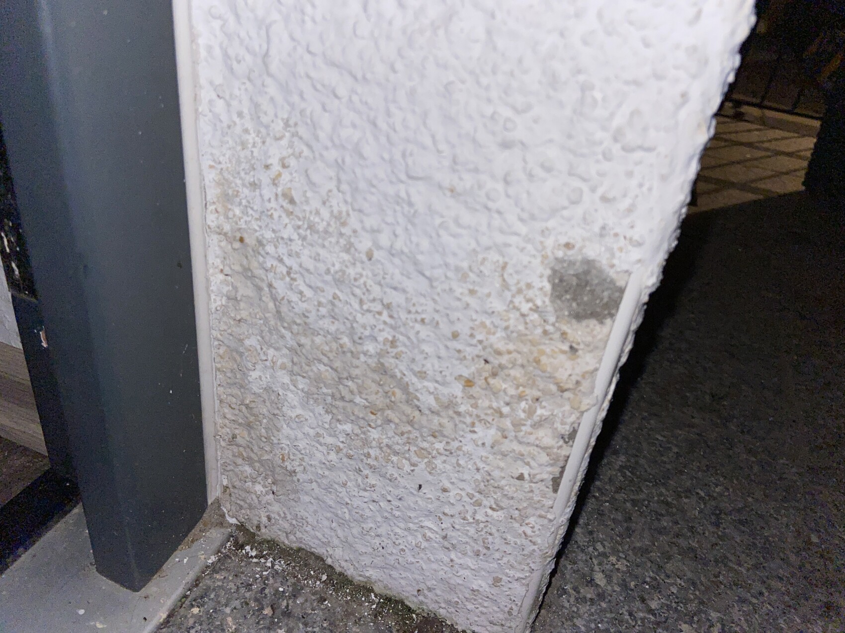 Säule mit rauer, weißer Putzoberfläche neben dunkler Metallkonstruktion bei Nacht
