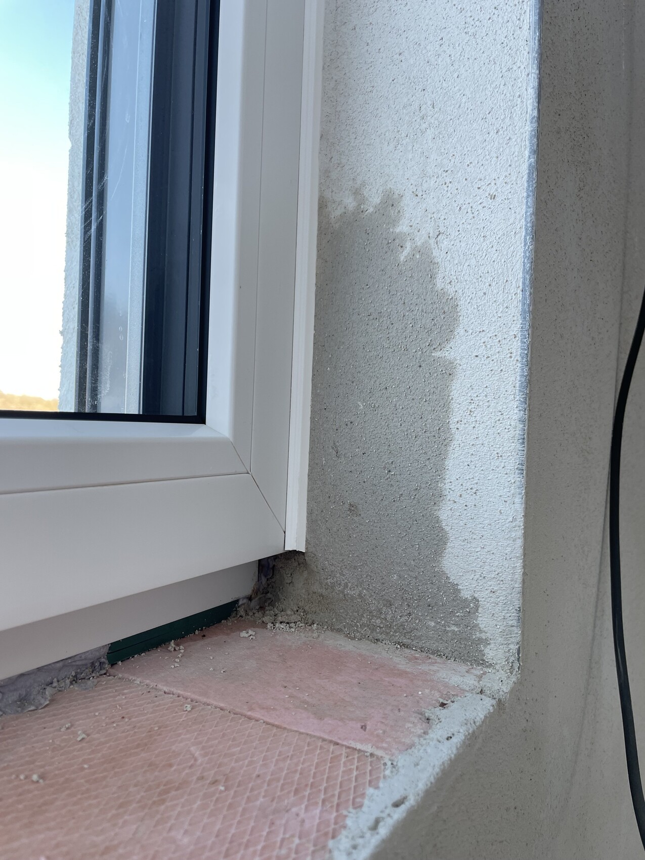 Außenwandbereich um Fenster mit beschädigtem Putz und Reparaturstellen