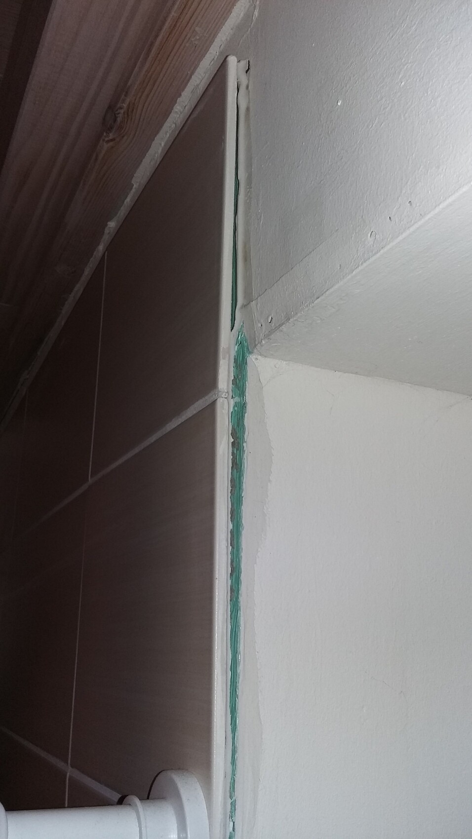 Nahaufnahme einer Fliesenkante im Bad mit grünem Dichtstoff an der Wand