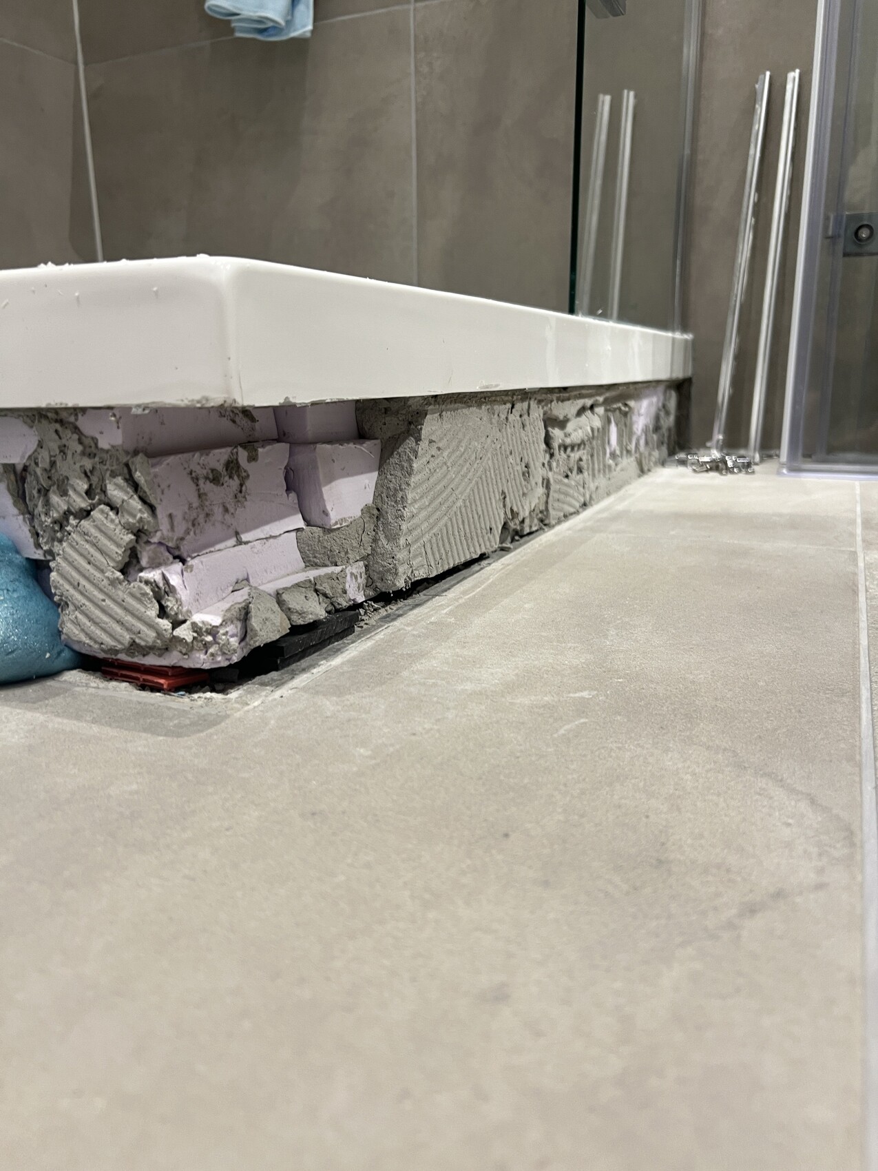 Freigelegter Unterbau unter der Badewanne: Beton und Styroporblöcke, Glasduschwand im Hintergrund.