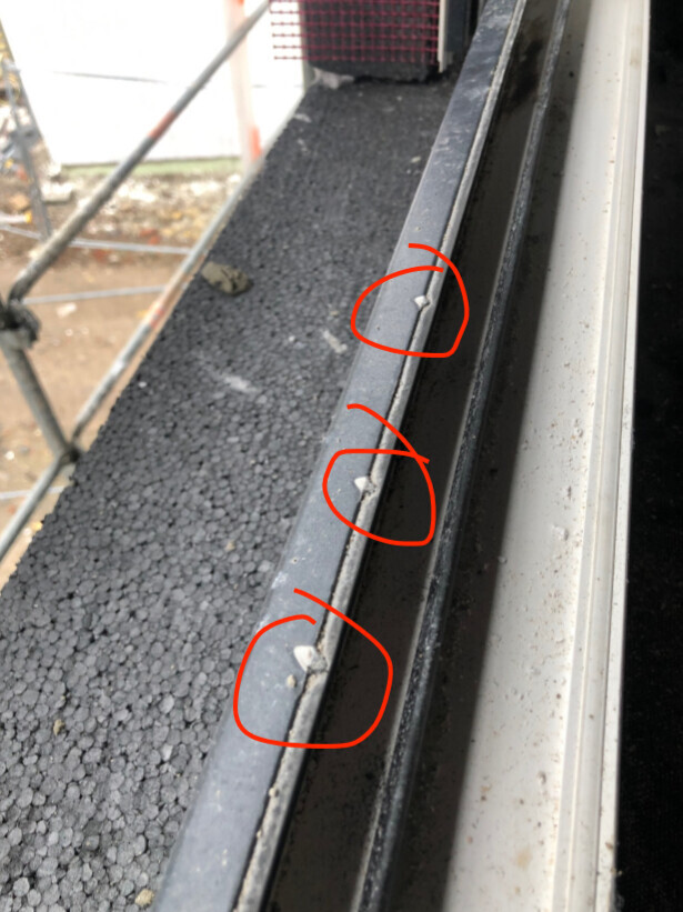 Nahaufnahme eines Metallgeländers mit weißen Clips, Baugerüst im Hintergrund