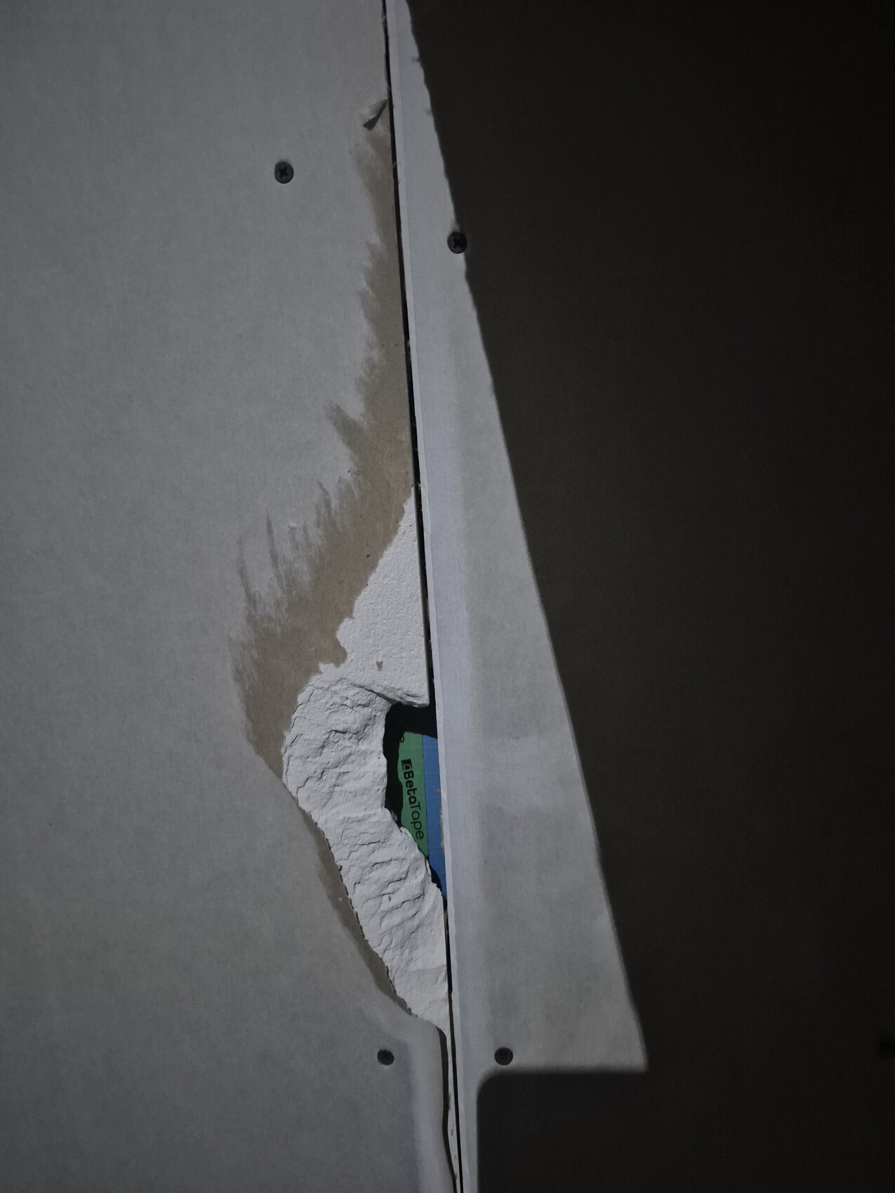 Beschädigte Trockenbauwand mit freigelegtem Putz und Schraubenköpfen