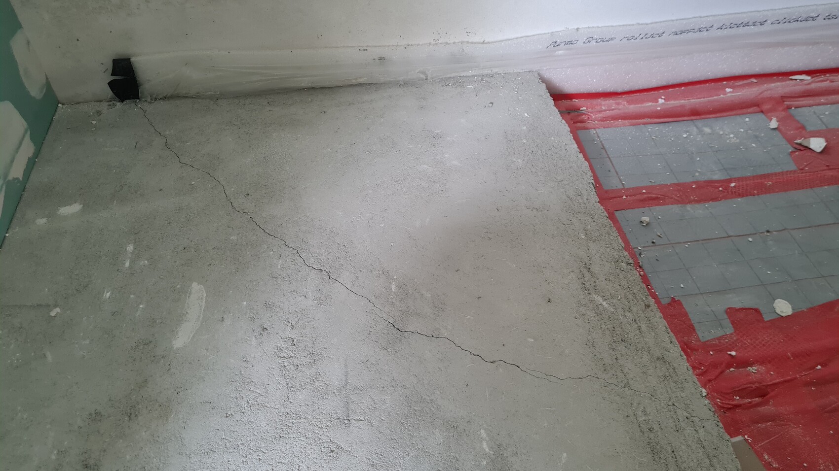 Rissiger Betonboden auf einer Baustelle; rote Dichtbahn am rechten Rand sichtbar.