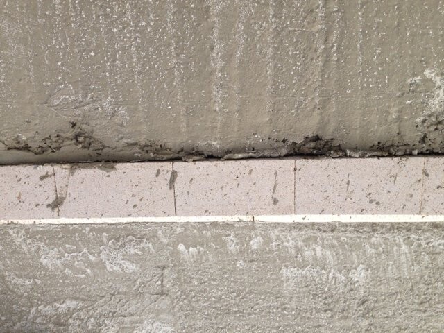 Nahaufnahme einer Betonwand-Bodenfuge mit Rissen und Baumängel.