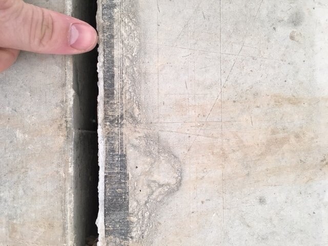 Nahaufnahme einer Betonkante mit Spalt und absplitterndem Rand, von einer Hand berührt