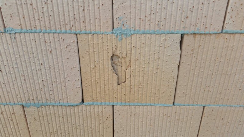Nahaufnahme eines beschädigten Porenbetonblocks mit Loch in der Wand