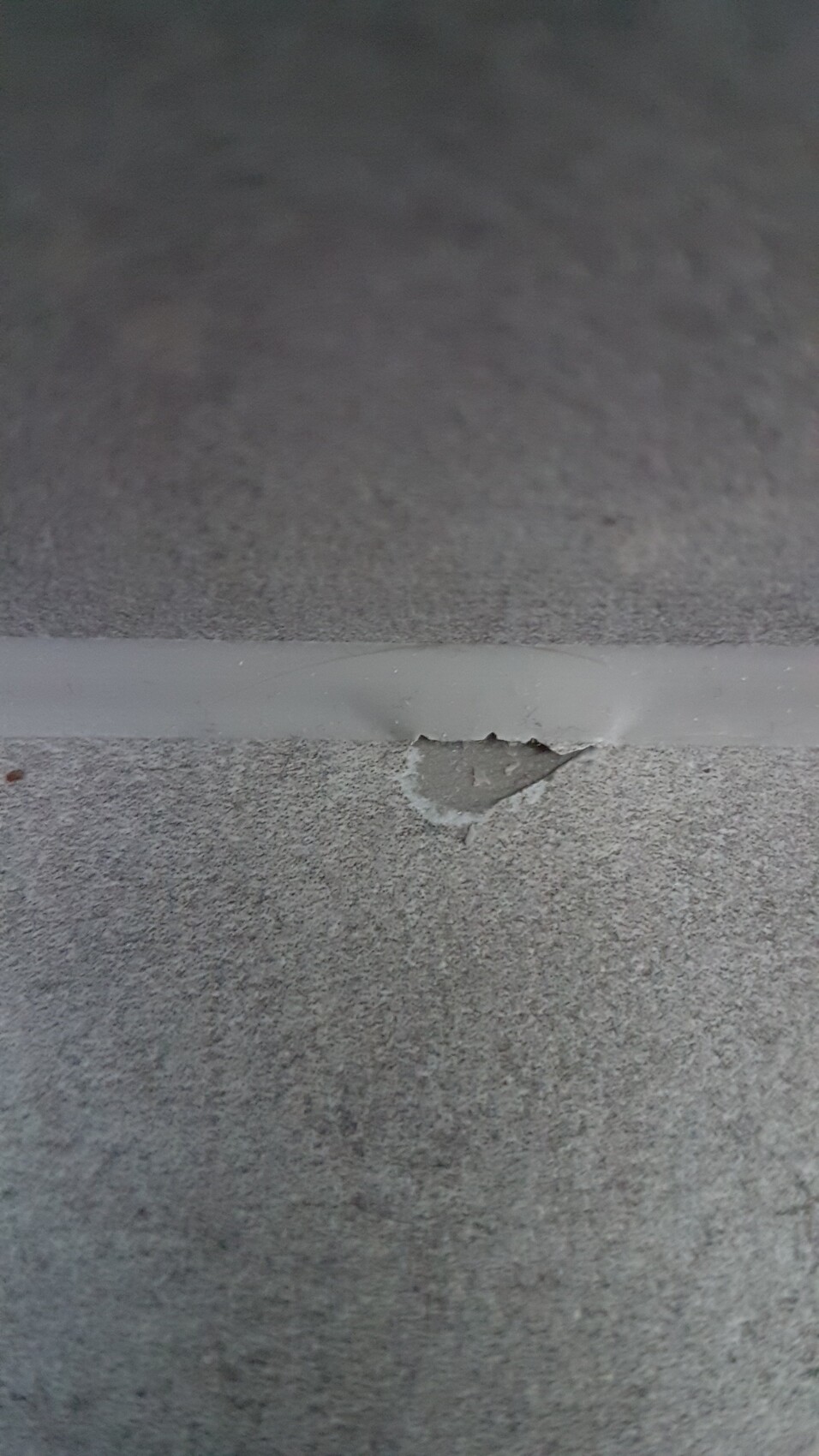 Grau betonierte Fläche mit dünnem hellgrauen Klebebandstreifen und einer kleinen Abplatzung.