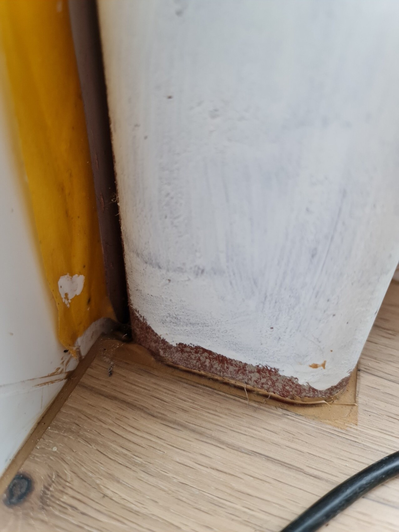Nahaufnahme einer weißen runden Stütze neben gelbem Türrahmen; abgeblätterte Farbe, Rost am Boden.