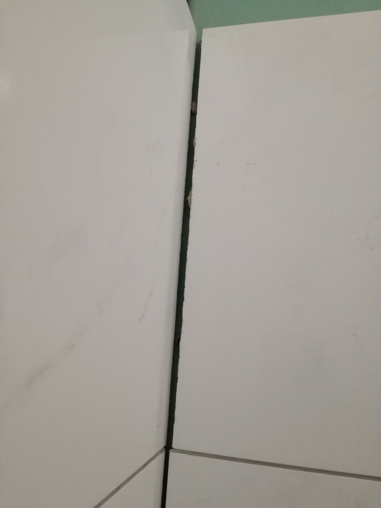 Nahaufnahme einer dunklen Spalte zwischen zwei weißen Fliesen.