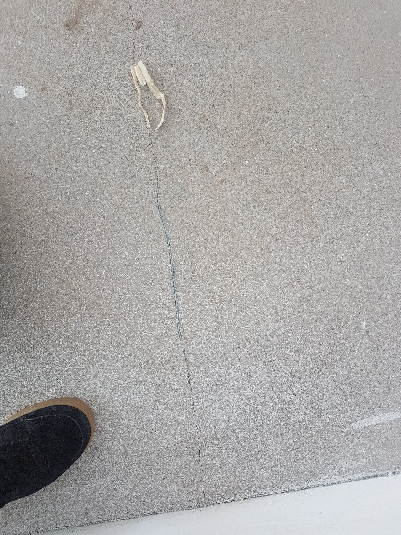 Blick auf Betonboden mit Riss; Schuh unten links, kleines helles Fragment auf dem Boden.