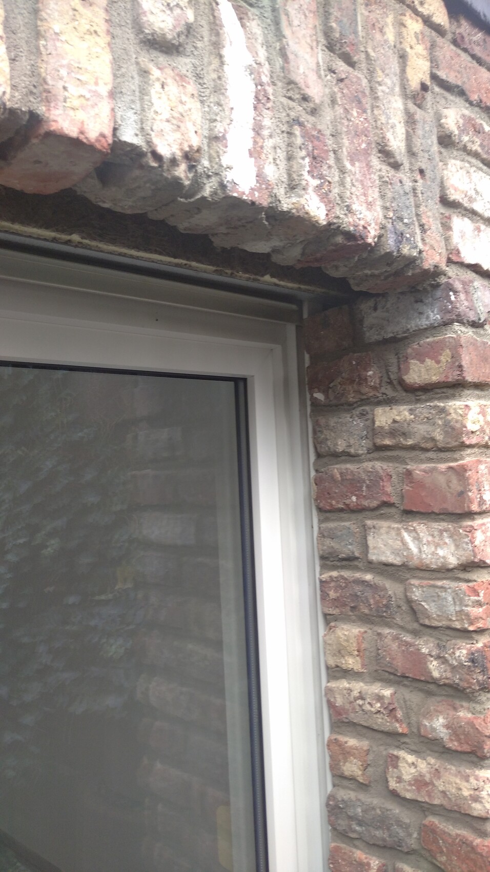 Weißer Fensterrahmen in roter Backsteinwand; sichtbar bröckelnder Mörtel über dem Fenster.