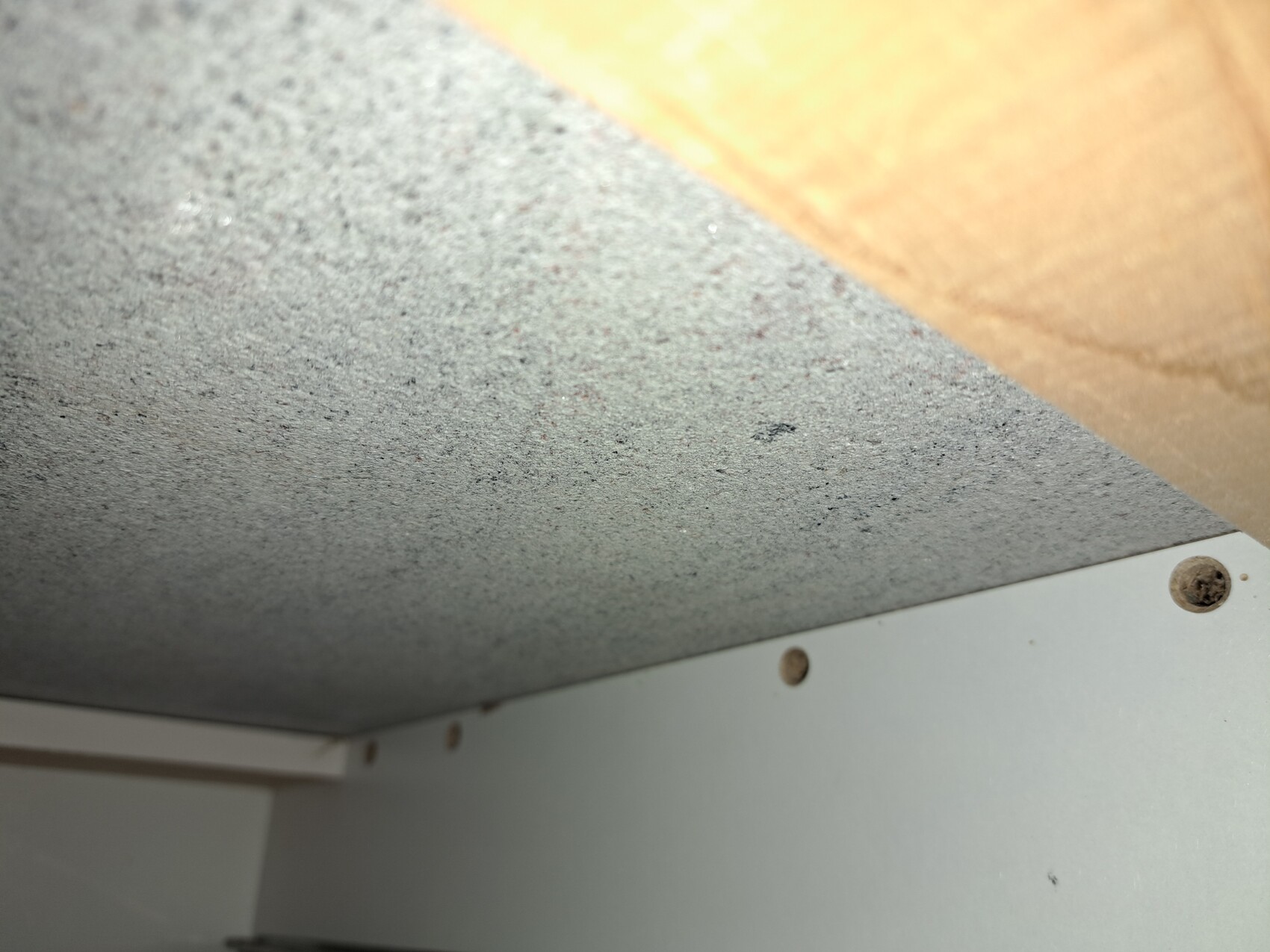 Nahaufnahme einer grauen, grob texturierten Platte unter einem Holzbalken; Schrauben sichtbar.