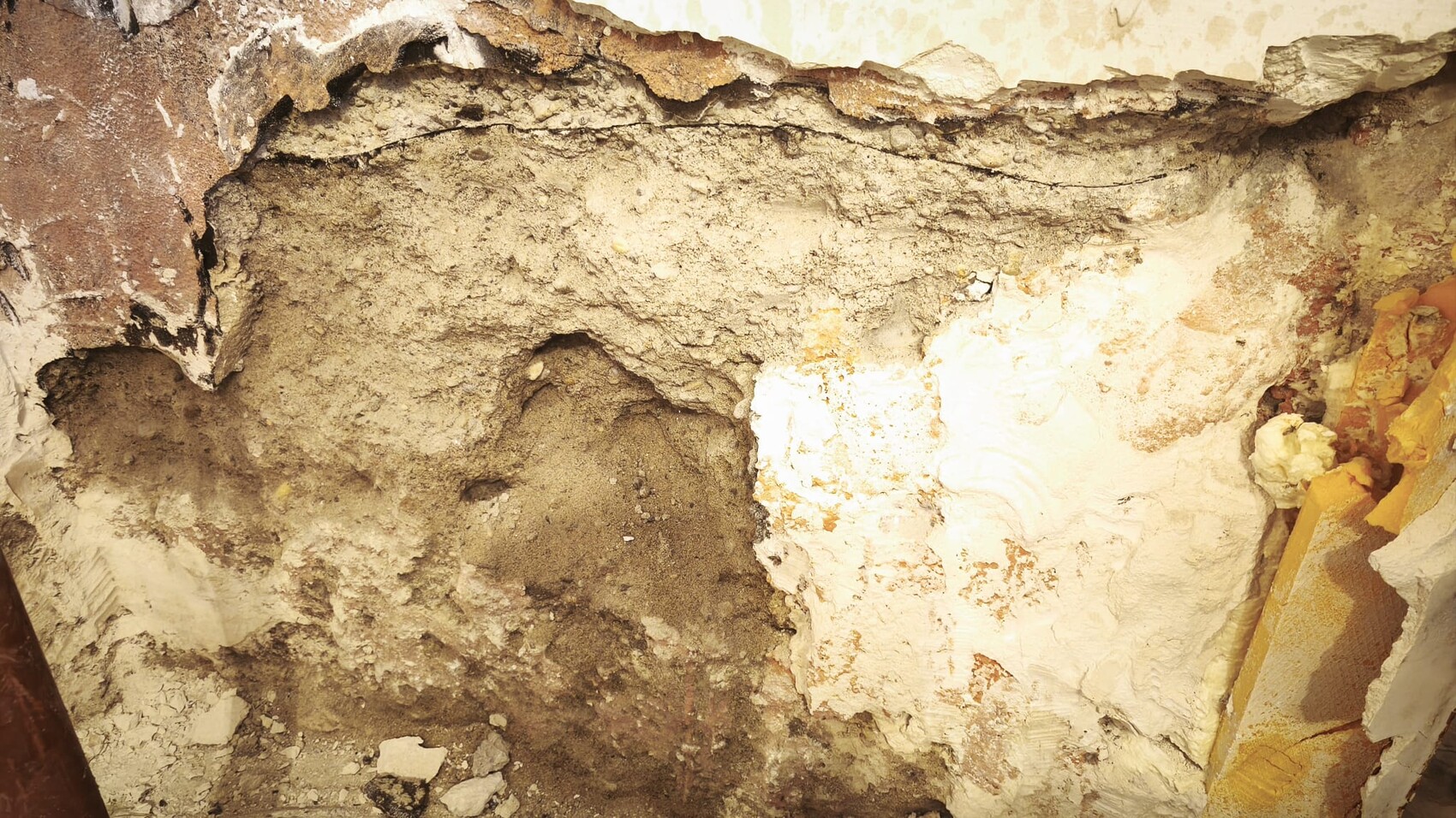 Exponierte Wand mit Putzbruch, erdiges Material und sichtbare Baumaengel im Innenbereich