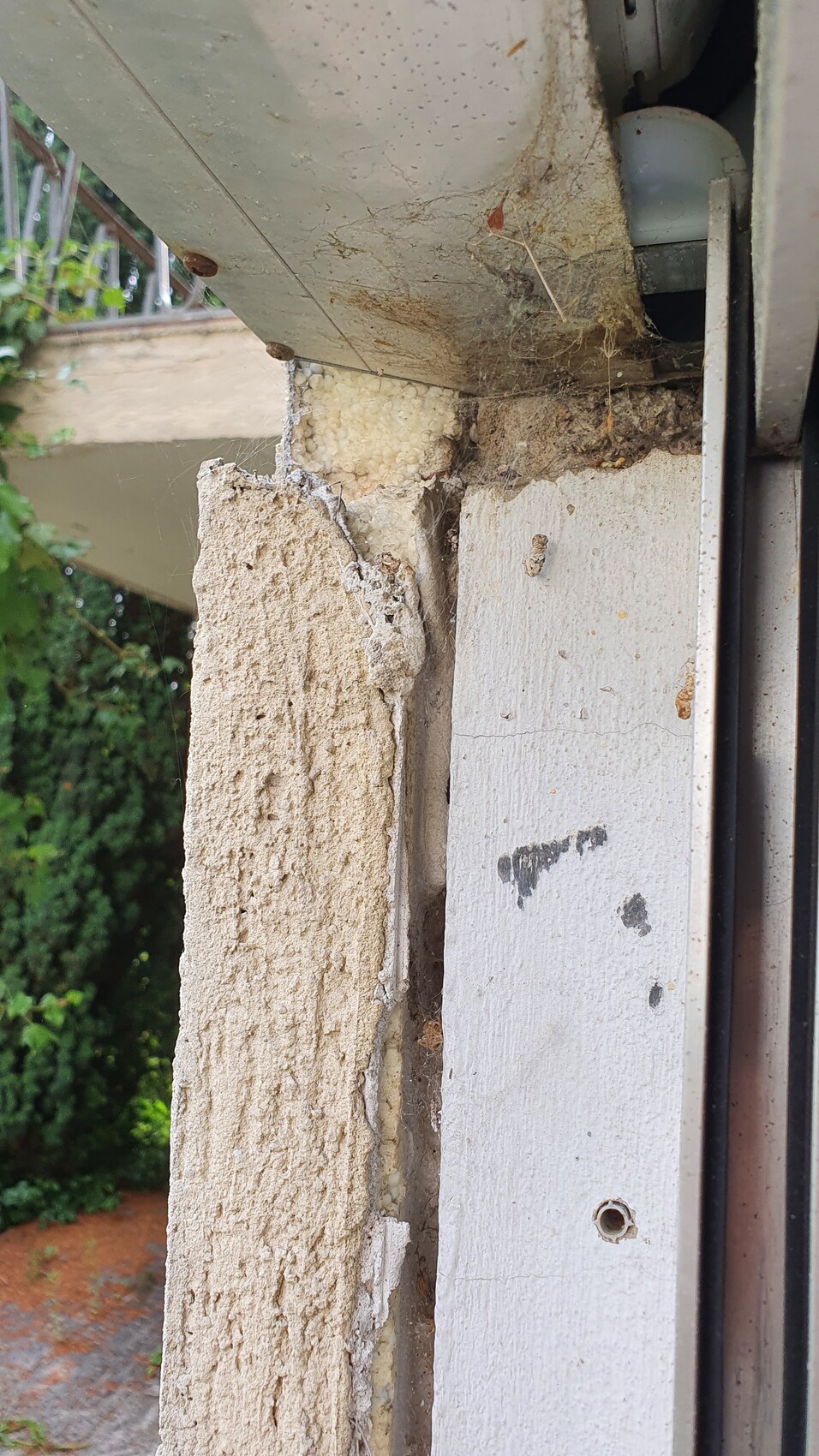Nahaufnahme einer beschädigten Außenwand: bröckelnder Putz, Dämmmaterial und Fensterrahmen sichtbar.