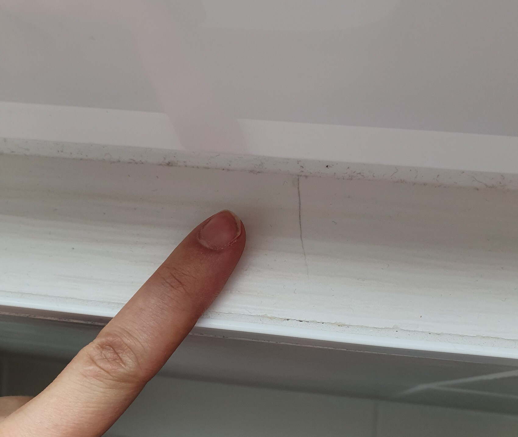 Nahaufnahme eines Fenstersims mit Riss und Staub, Finger zeigt Baumängel