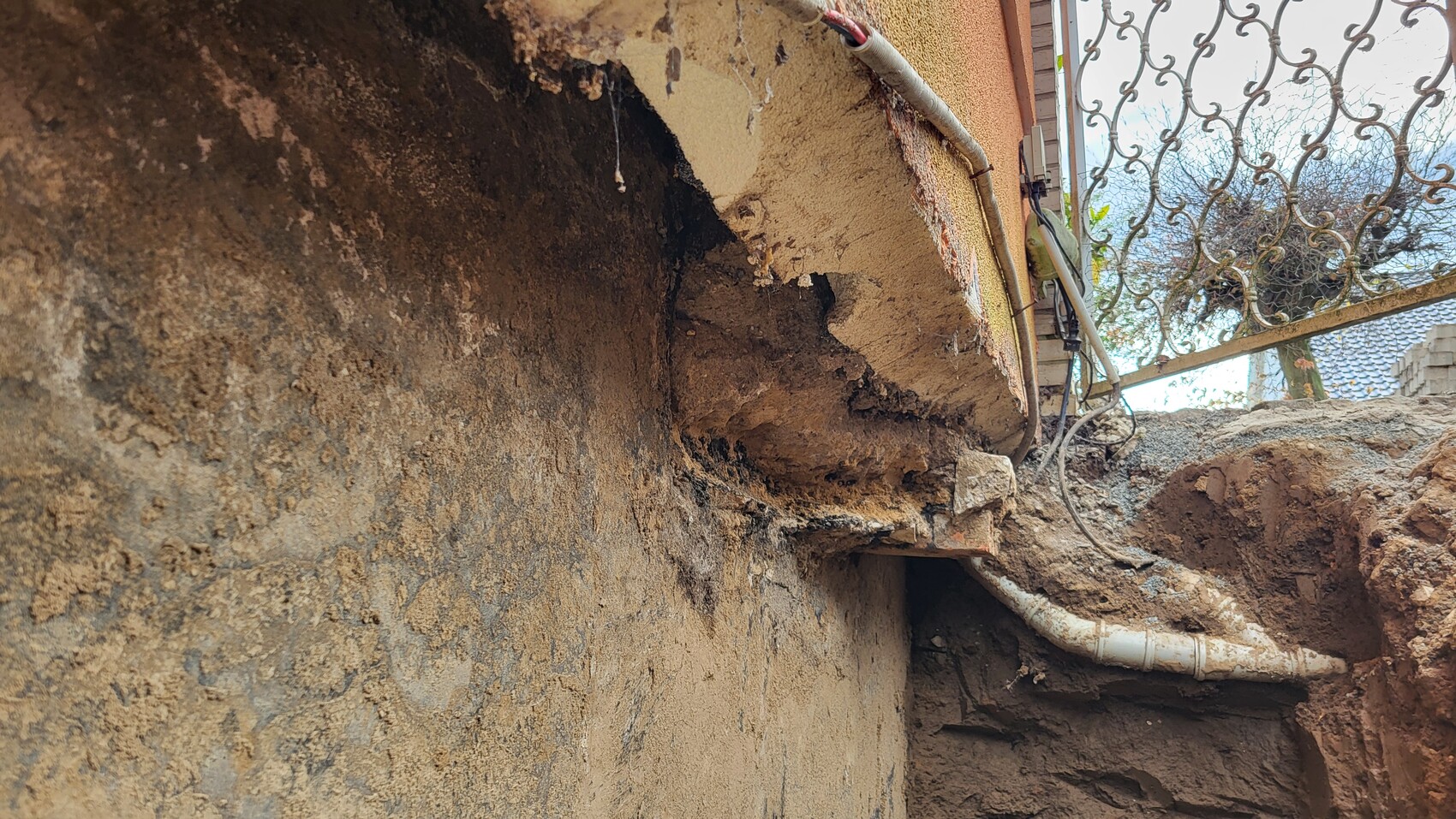 Außenwand mit Erdreich, Putzbruch und Grubenaushub; sichtbare Rohre