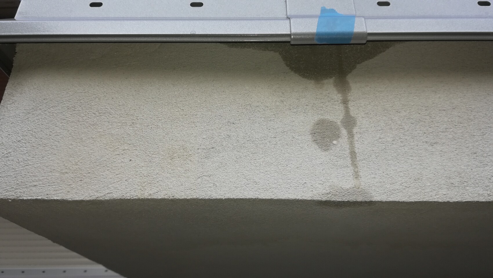 Beiger Teppichboden mit nassem Fleck und Wasserstreifen unter Metallkante; blaues Klebeband.