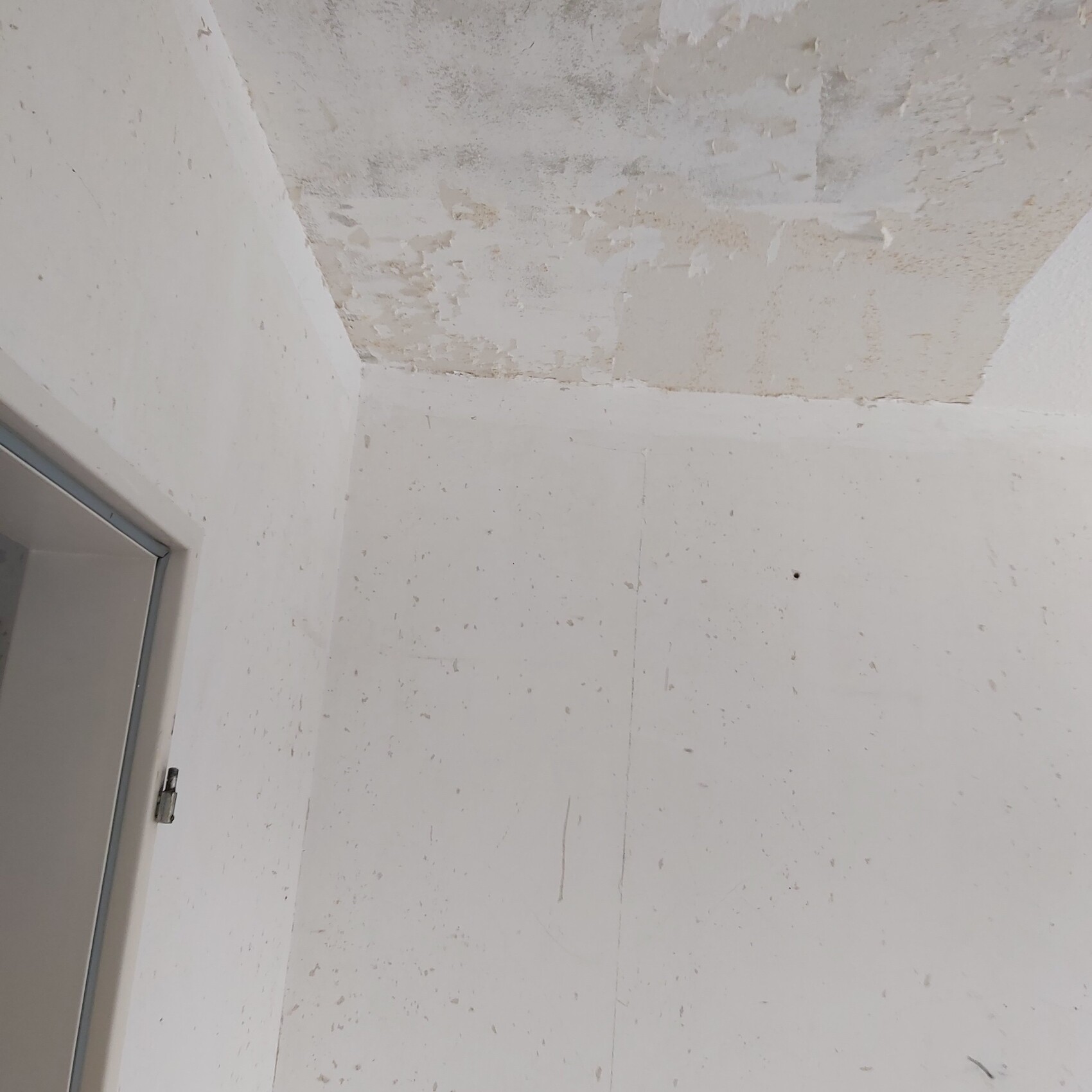 Ecke eines renovierungsbedürftigen Raums mit abgeblättertem Putz an Decke und Wand