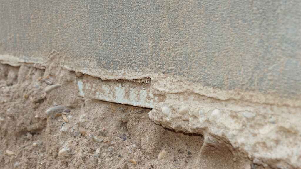 Nahaufnahme eines freigelegten Fundaments mit Erdreich und beschädigter Mauerkante.