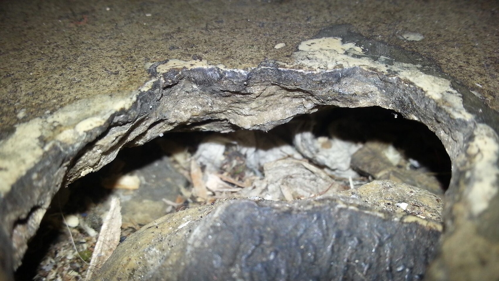 Nahaufnahme eines Lochs in einer Betonoberfläche mit Bröseln und Staub