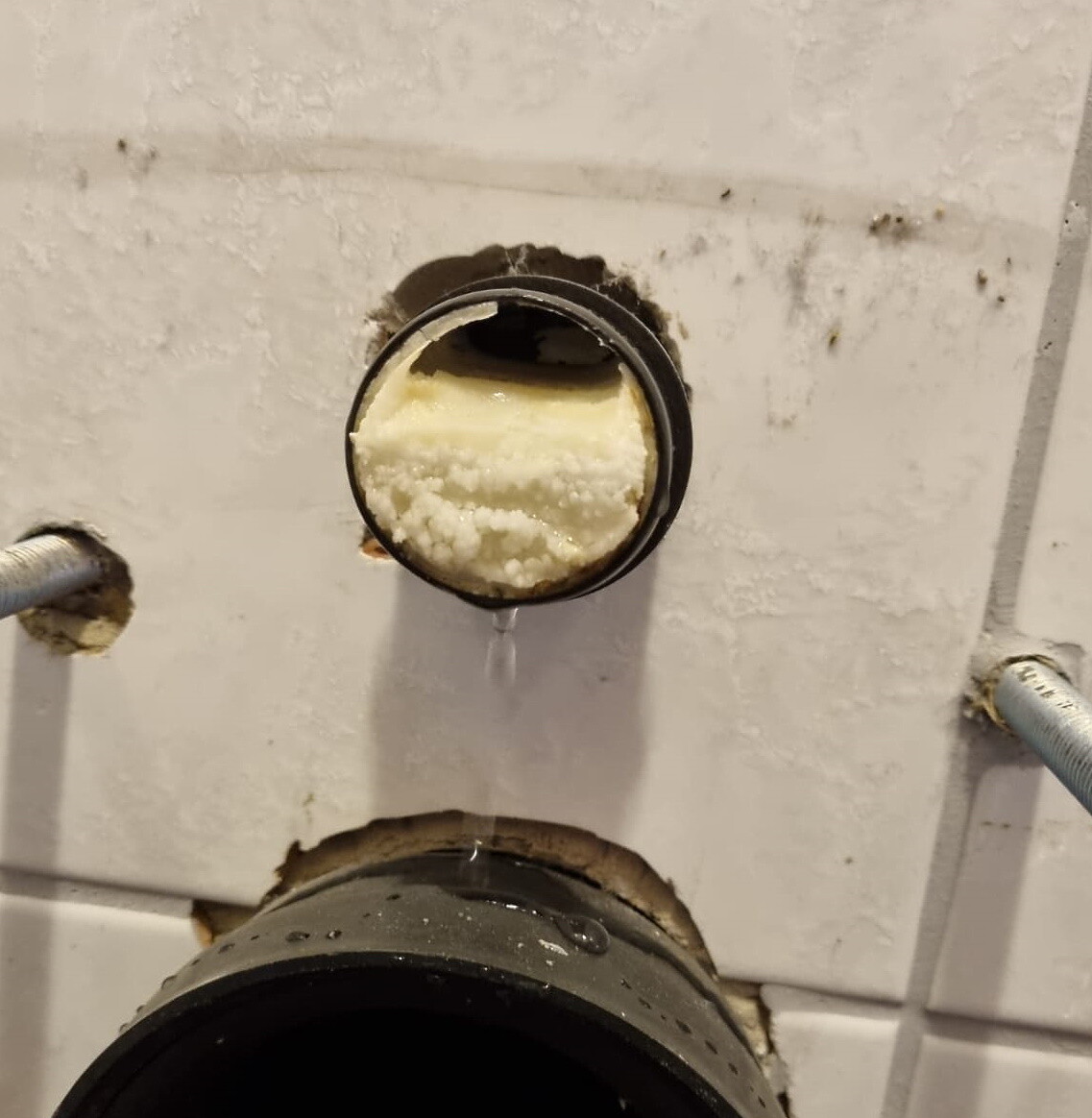Offenes Sanitärrohr mit Schaumdichtung, Wasser tropft aus dem Anschluss vor Fliesen.