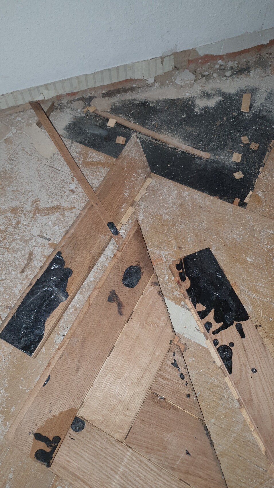 Zerlegter Boden mit verstreuten Holzbrettern und schwarzen Klebe-Teer-Spuren.