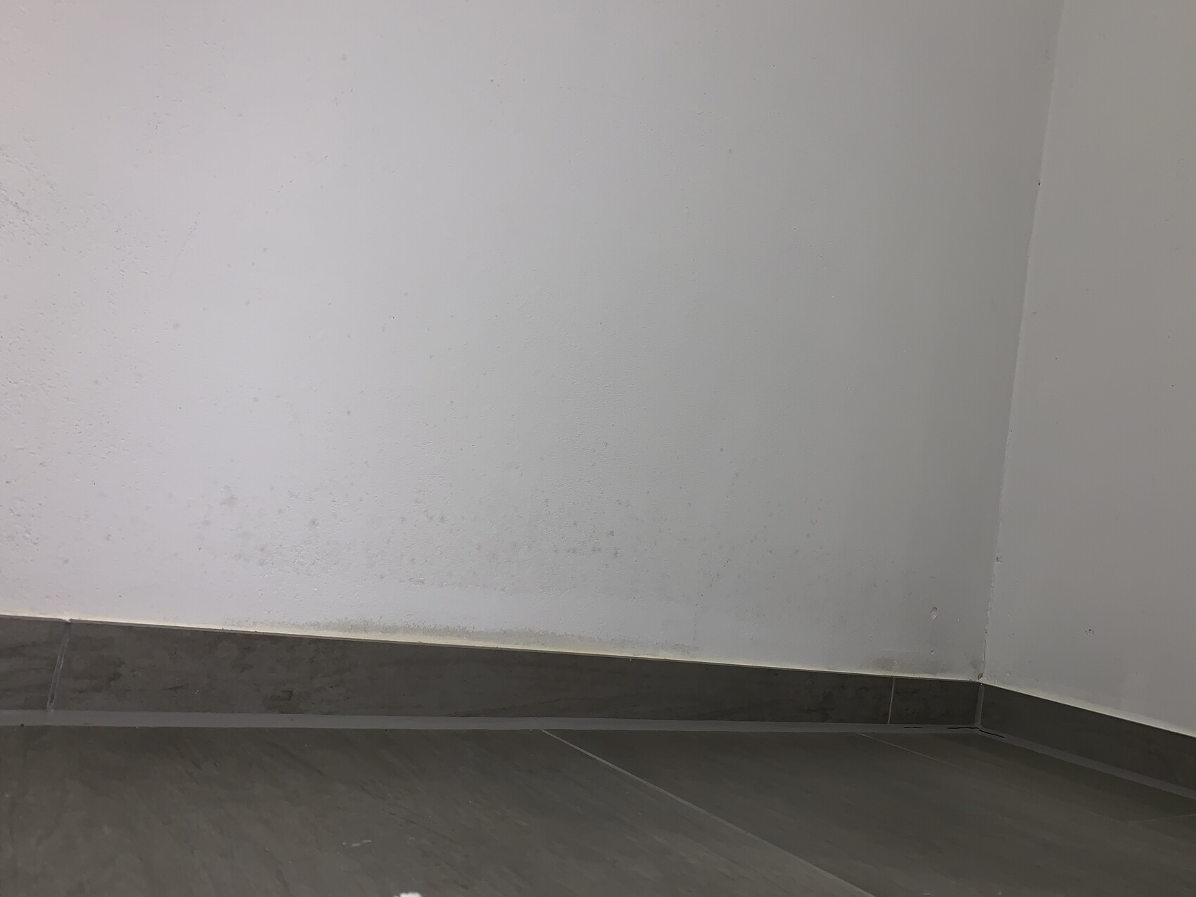 Ecke eines Innenraums mit weißen Wänden und Bodenleiste, Feuchtigkeitsschatten am unteren Wandbereich