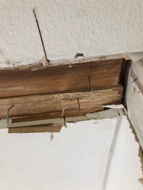 Sicht auf eine beschädigte Decke/Wand: freiliegter Holzbalken, Nägel und bröckelnder Putz.