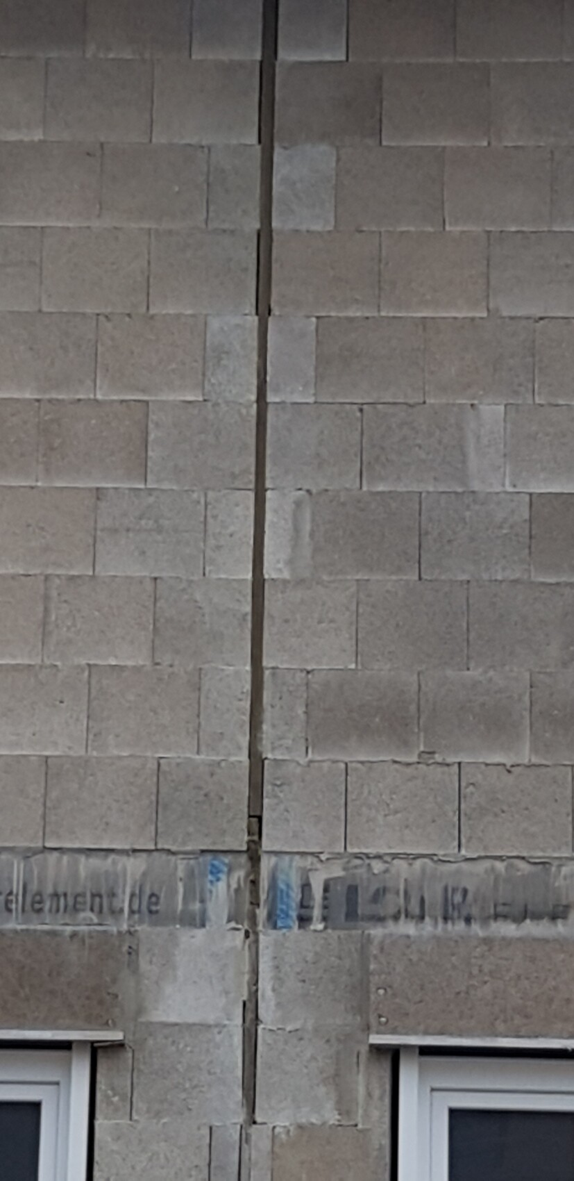 Graue Steinwand mit einem vertikalen Spalt in der Mitte; unten zwei Fenster.